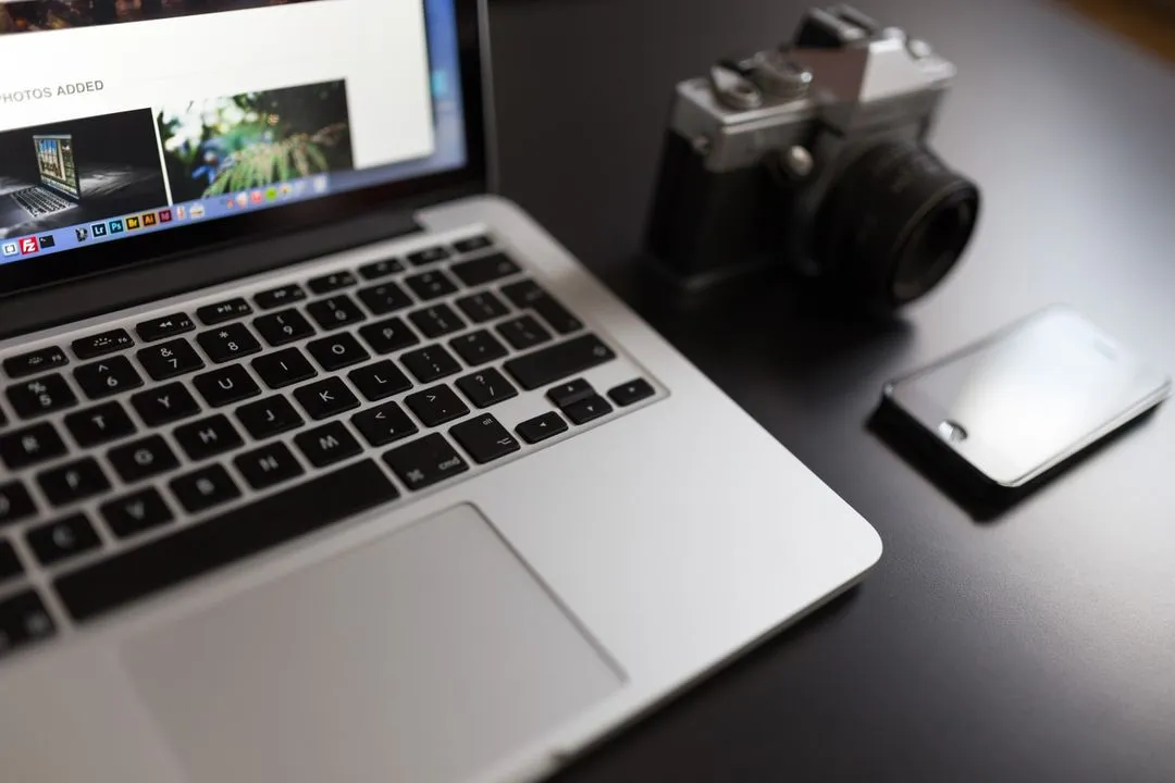 Image of an opened laptop next to a smartphone and a camera on a table - The beginner's guide to YouTube marketing, how to increase subscribers quickly - Image