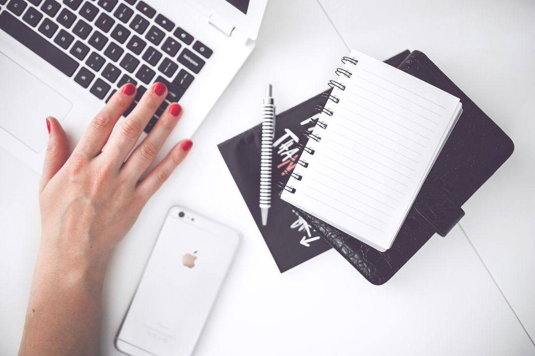 Image of a woman with red painted nails working on a laptop with a notebook and a phone next to it - 25 useful social media marketing ideas for boosting engagement - Image