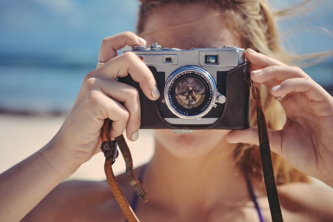 Close up of a woman holding a camera up over her face, taking a photo on a beach