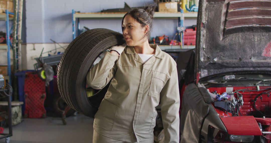 Image of happy biracial female car mechanic holding tyre - Free Images, Stock Photos and Pictures on Pikwizard.com