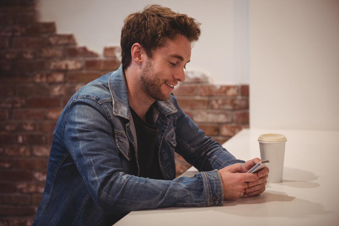 Image of a Man Using his Mobile Phone at a Table and Smiling