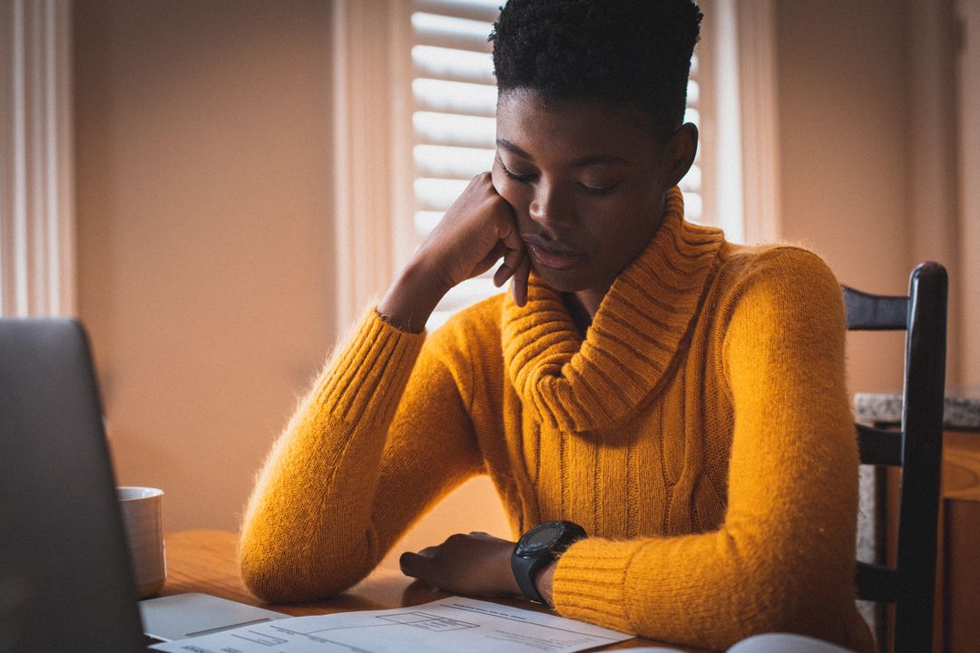 Woman sitting infront of a laptop, looking down at some papers - Expert online marketing tips to improve your digital strategy and make more money - Image