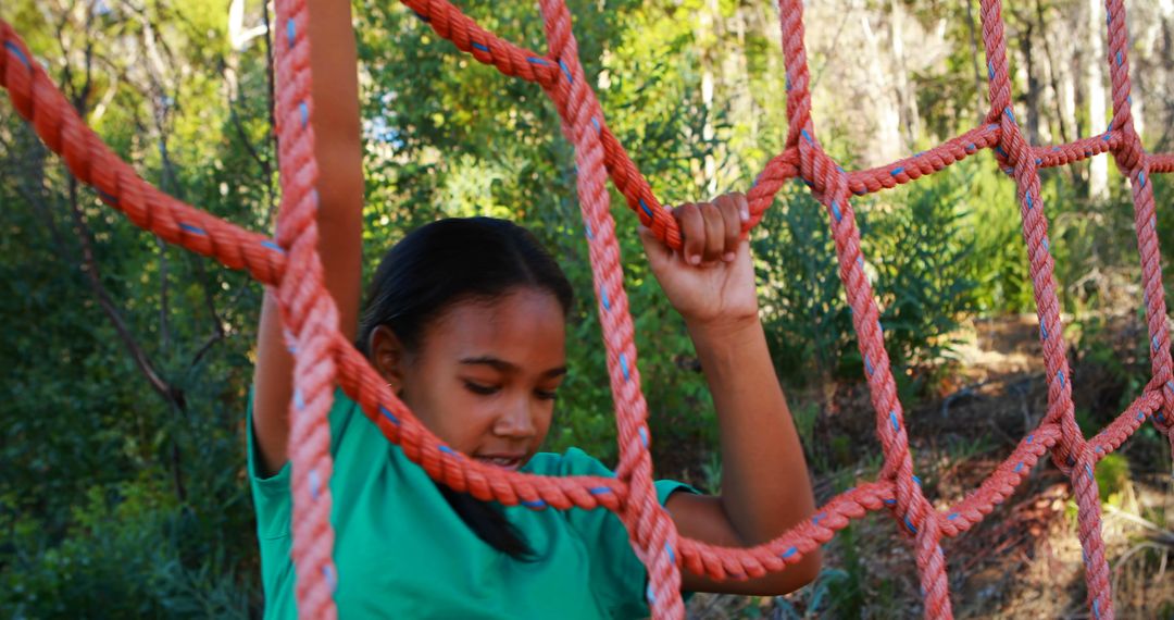A young girl is engaged in climbing a red rope net at an outdoor playground,  with copy space from Pikwizard