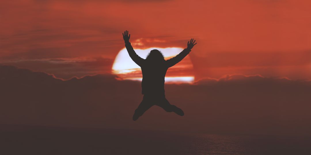 silhouette of a person jumping in front of a red sunset 