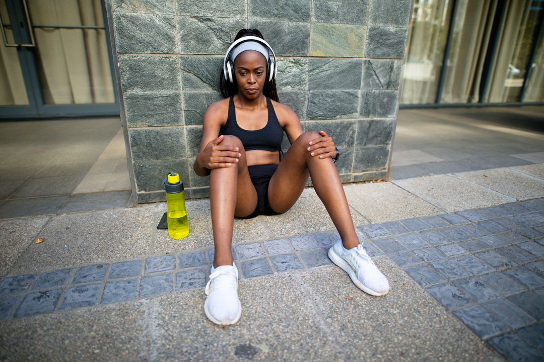 A woman in athletic attire is seen inserting earphones while exercising  outdoors. from Pikwizard