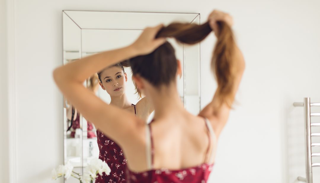 Image of a Woman Tying her Hair Up in Front of the Mirror in the Bathroom