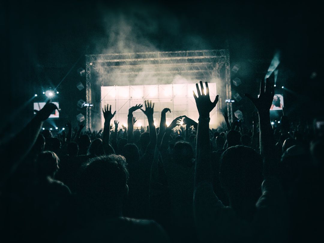 Image of a crowd at a concert with their hands up with the stage lit