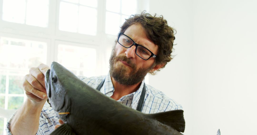 A middle-aged Caucasian man examines a large fish with a curious  expression, with copy space from Pikwizard