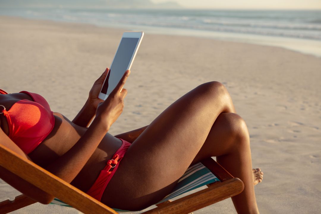 Woman using digital tablet while relaxing in a beach chair on the beach - Free Images, Stock Photos and Pictures on Pikwizard.com