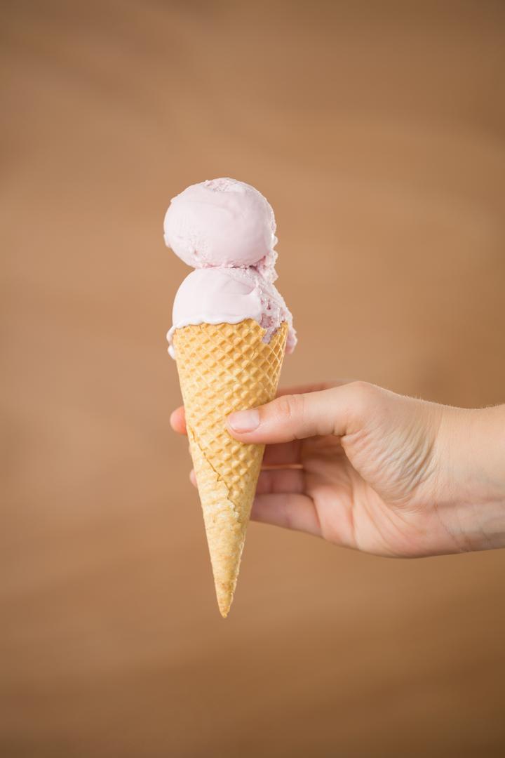 Hand holding a waffle cone with double scoop strawberry ice cream