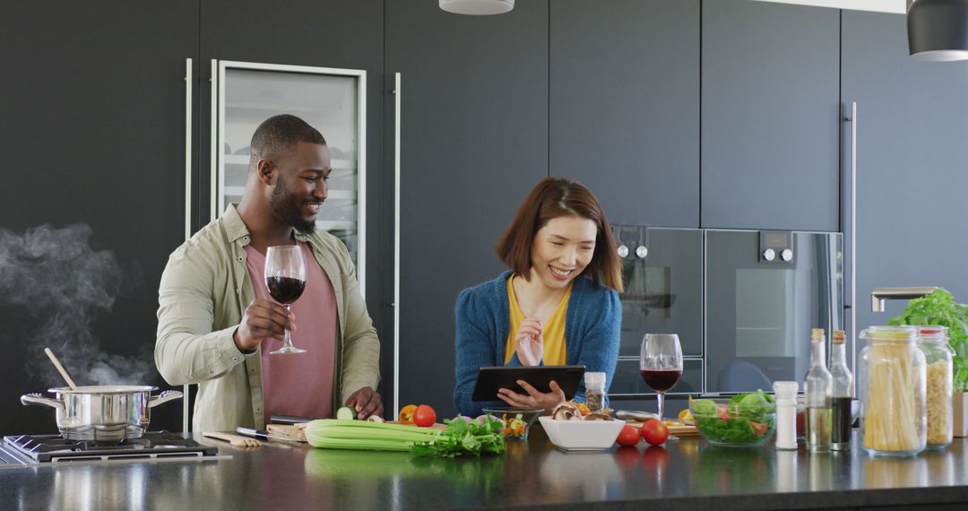 Image of happy diverse couple preparing food making a toast and using tablet in kitchen at home - Free Images, Stock Photos and Pictures on Pikwizard.com