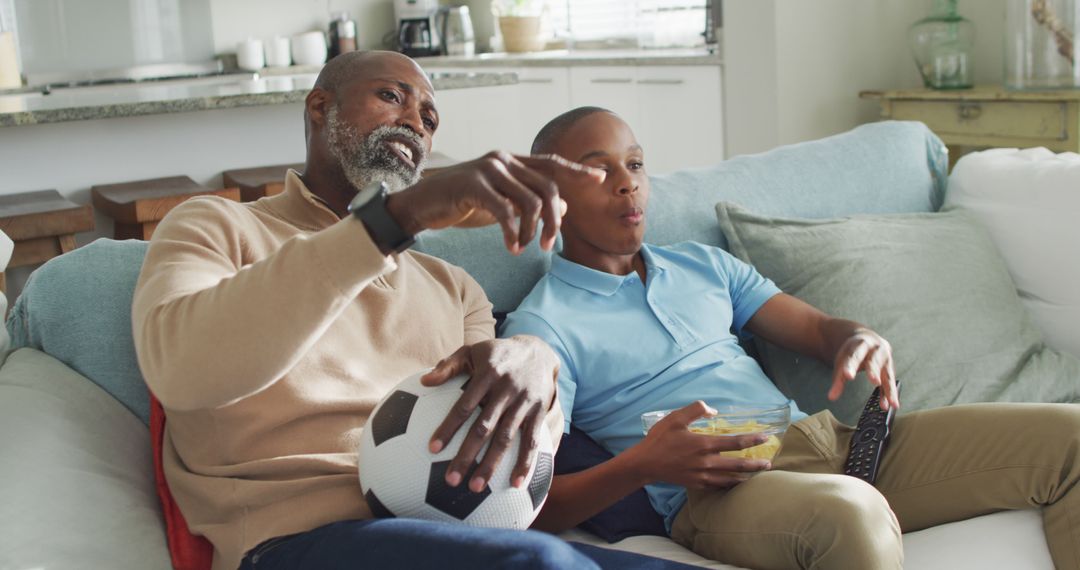 Image of happy african american father and son eating chips and watching tv together - Free Images, Stock Photos and Pictures on Pikwizard.com