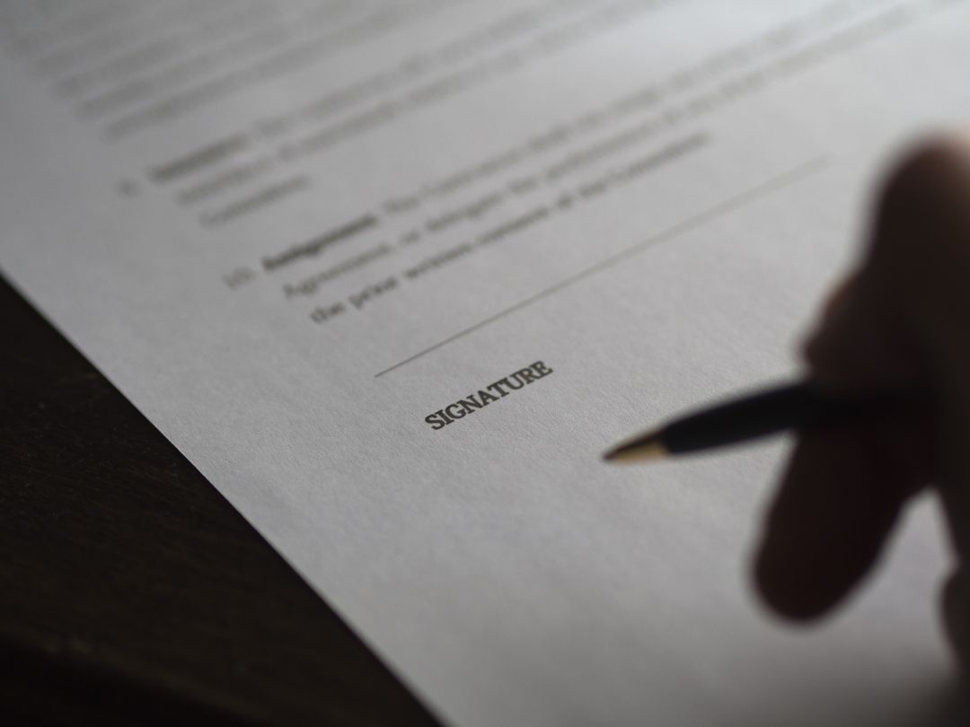 Image of a Person Holding a Pen over the Signature Section of a Blurred Contract