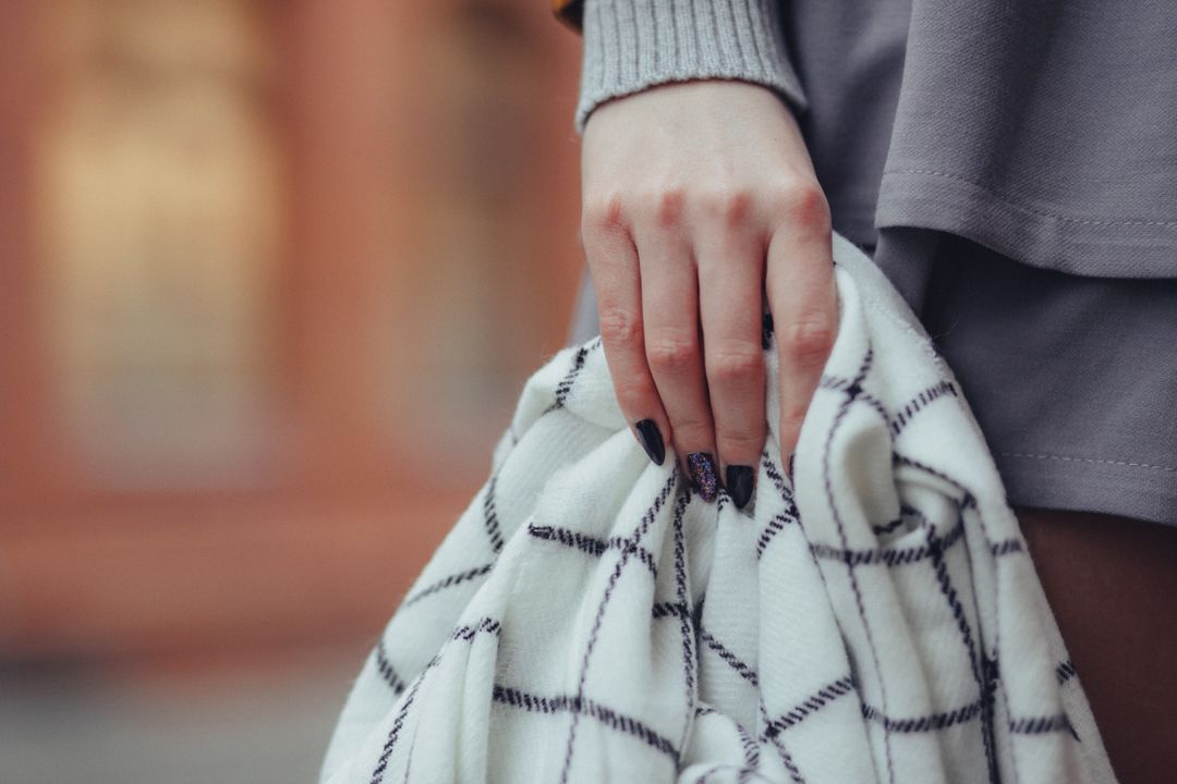 Woman holding a black and white scarf with long nails in a urban street