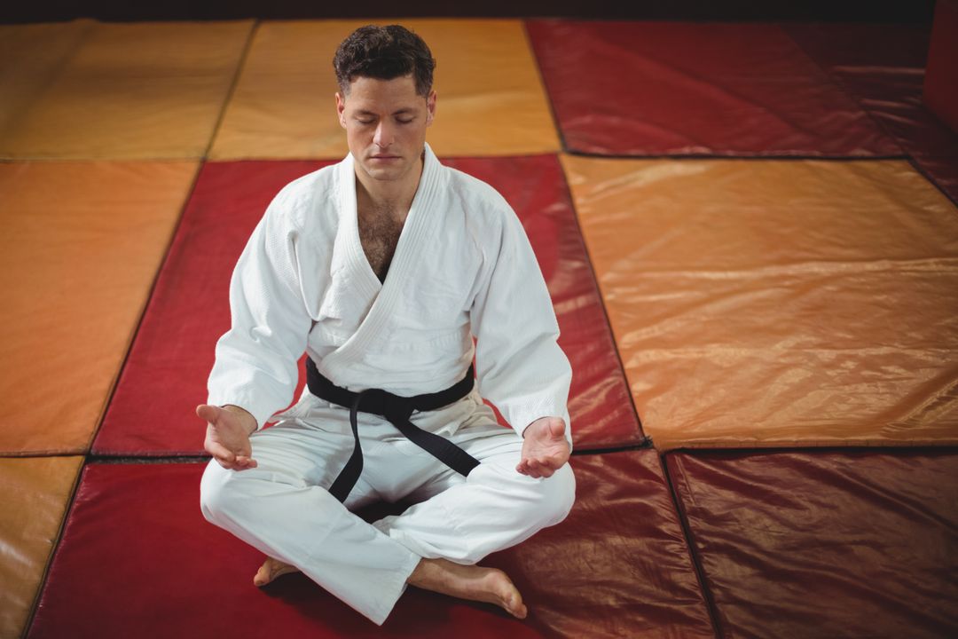 Man meditating on a gym floor wearing a black belt