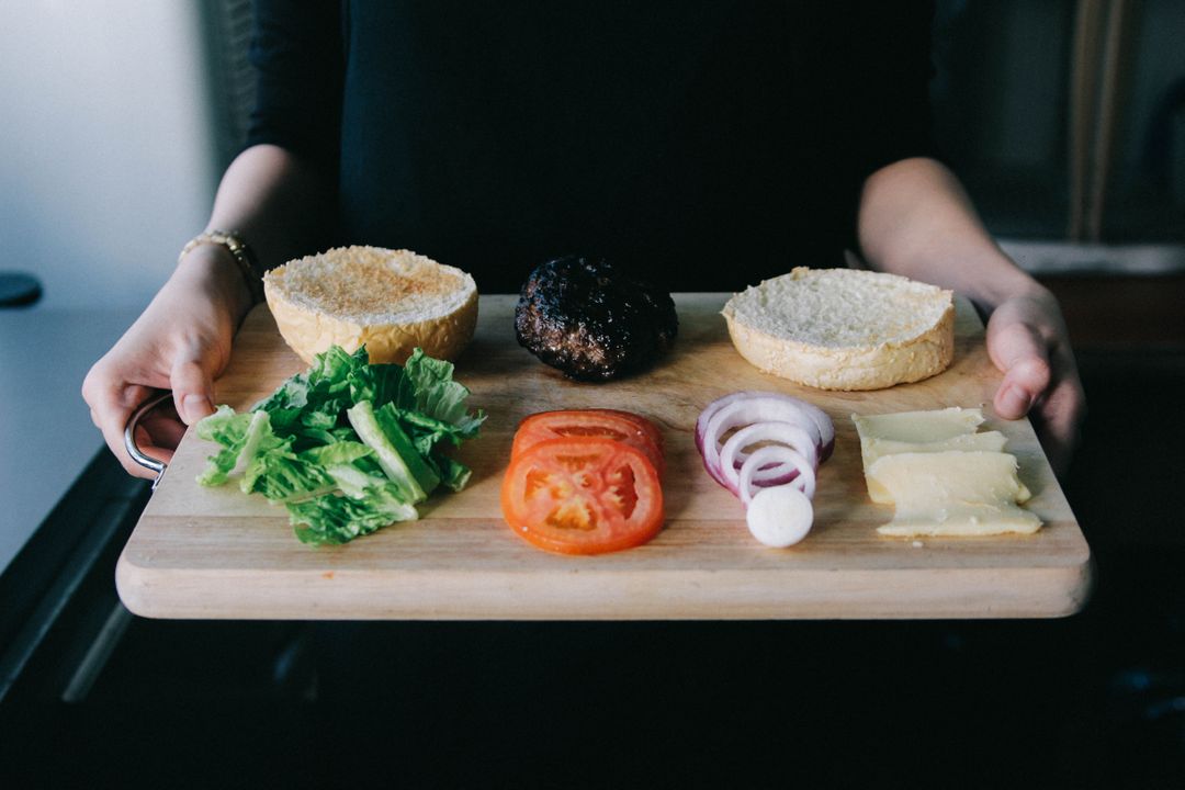 a person holding a cutting board with hamburger, onion, tomato, and cheese - Free Images, Stock Photos and Pictures on Pikwizard.com