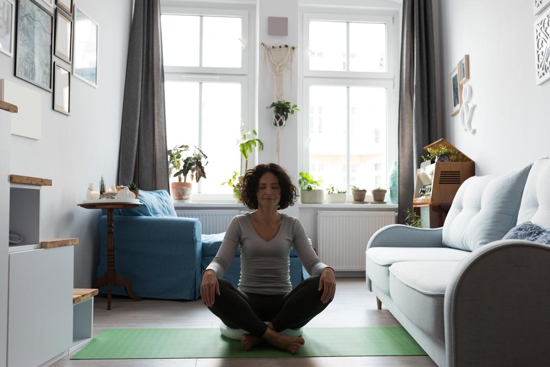 Woman doing yoga on a green mat in her living room, windows in the background