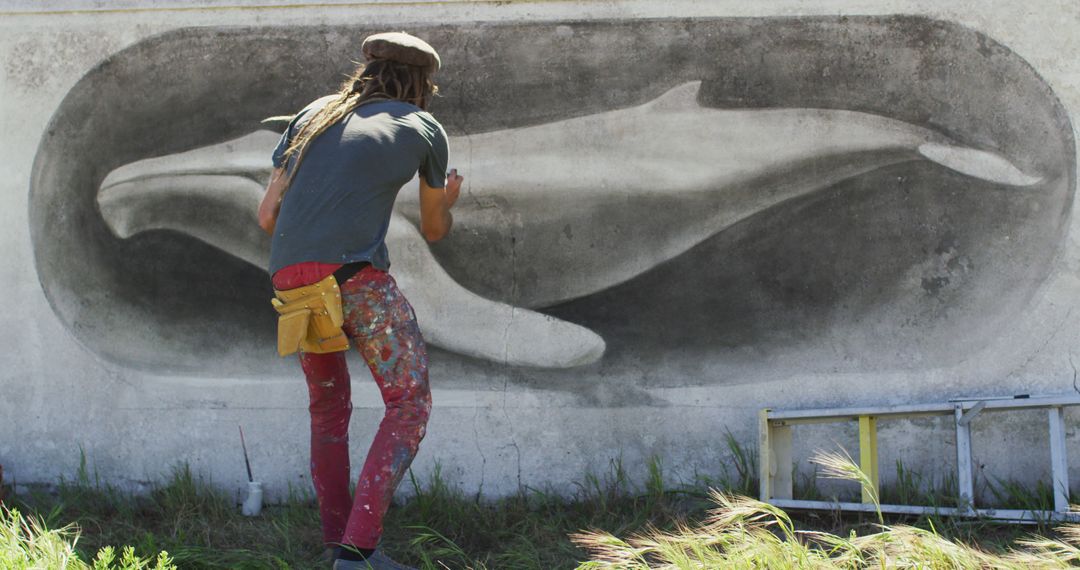 Image of rear view of caucasian male artist with dreadlocks painting whale mural on wall - Free Images, Stock Photos and Pictures on Pikwizard.com
