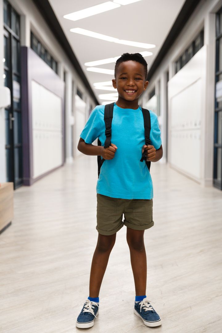 Portrait of smiling african american elementary schoolboy with backpack standing in school corridor - Free Images, Stock Photos and Pictures on Pikwizard.com