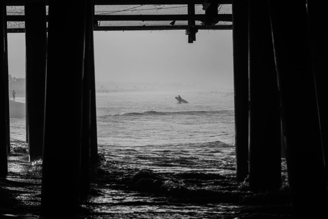 a surfer under a pier - Free Images, Stock Photos and Pictures on Pikwizard.com