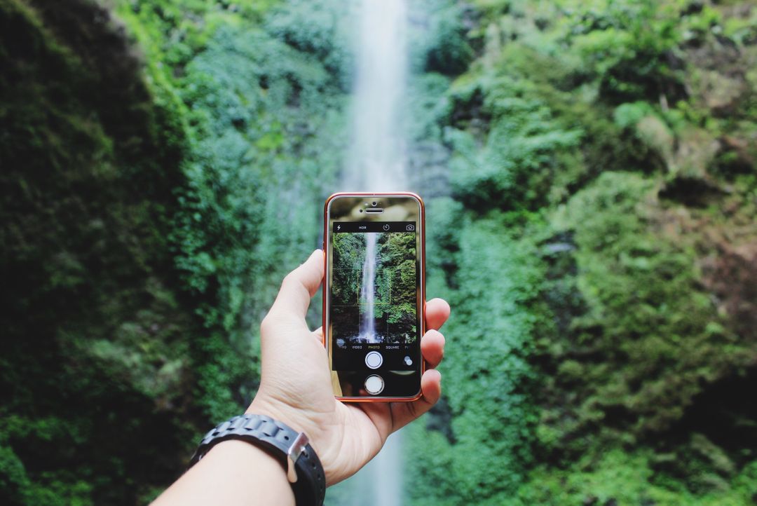 Man taking a picture of a waterfall on his smartphone