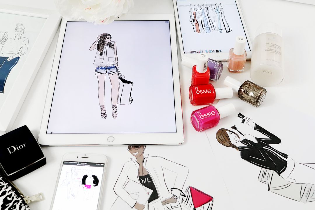 Tablet with fashion drawing on a table surrounded by nailpolish and graphics