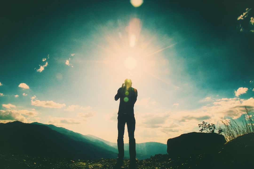 a man standing on a mountain top with the sun shining through the clouds - Free Images, Stock Photos and Pictures on Pikwizard.com