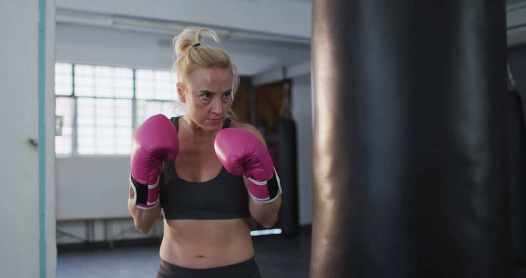 Caucasian female boxer wearing boxing gloves training with punching bag at  the gym from Pikwizard