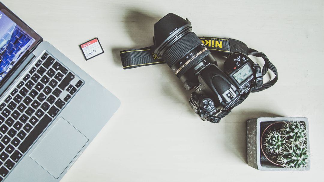 Overhead image of a laptop, sd card, camera and a cactus plant on a wooden desk - A complete beginner's guide on how to post on Instagram from a PC or Mac - Image