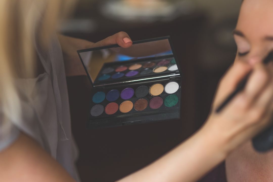 Image of a woman getting her makeup done, with applier holding an eyeshadow palette thats in focus
