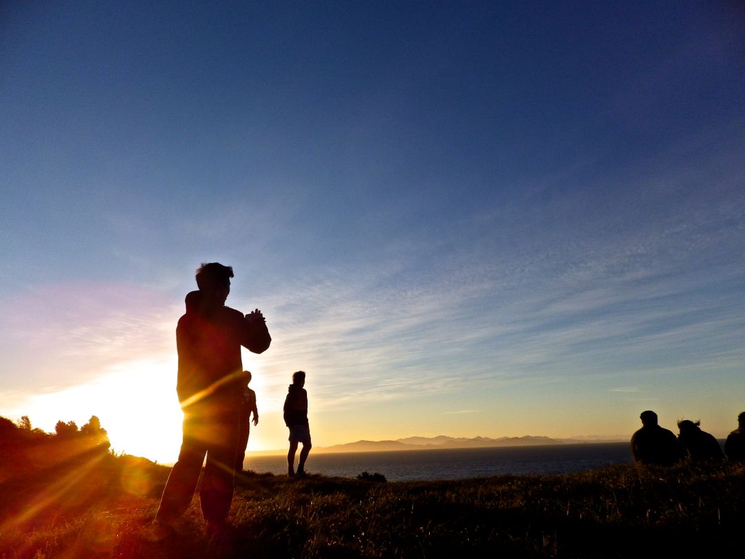 Family of hikers standing on a cliff watching the sunset