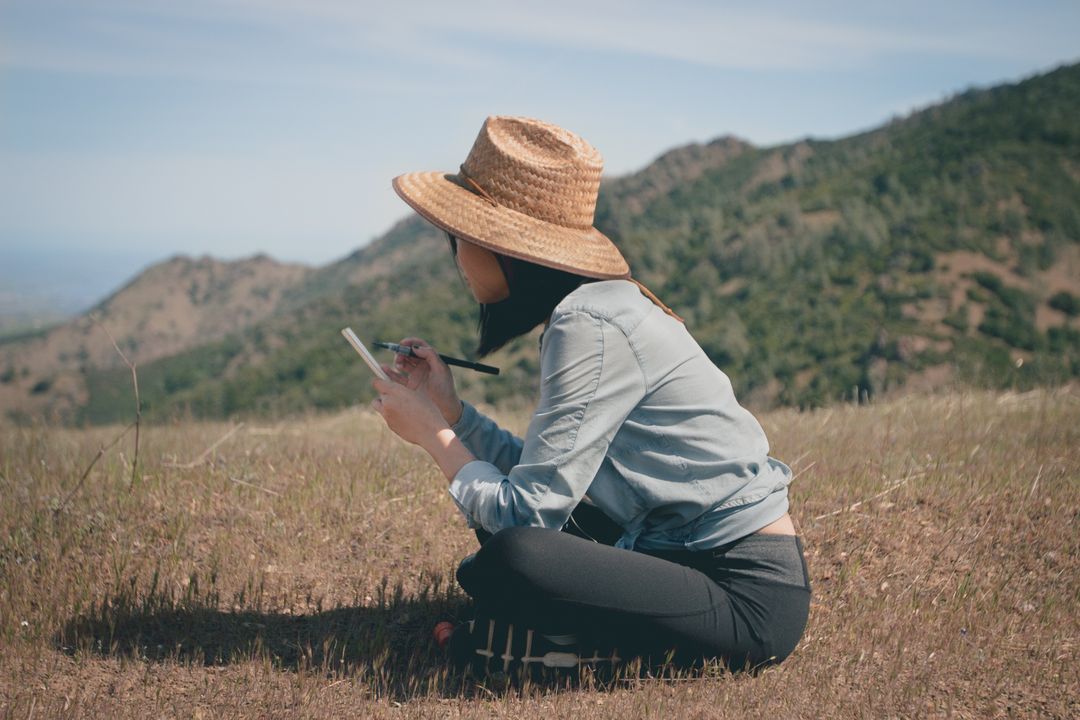 a woman sitting on a hill with a hat on - Free Images, Stock Photos and Pictures on Pikwizard.com