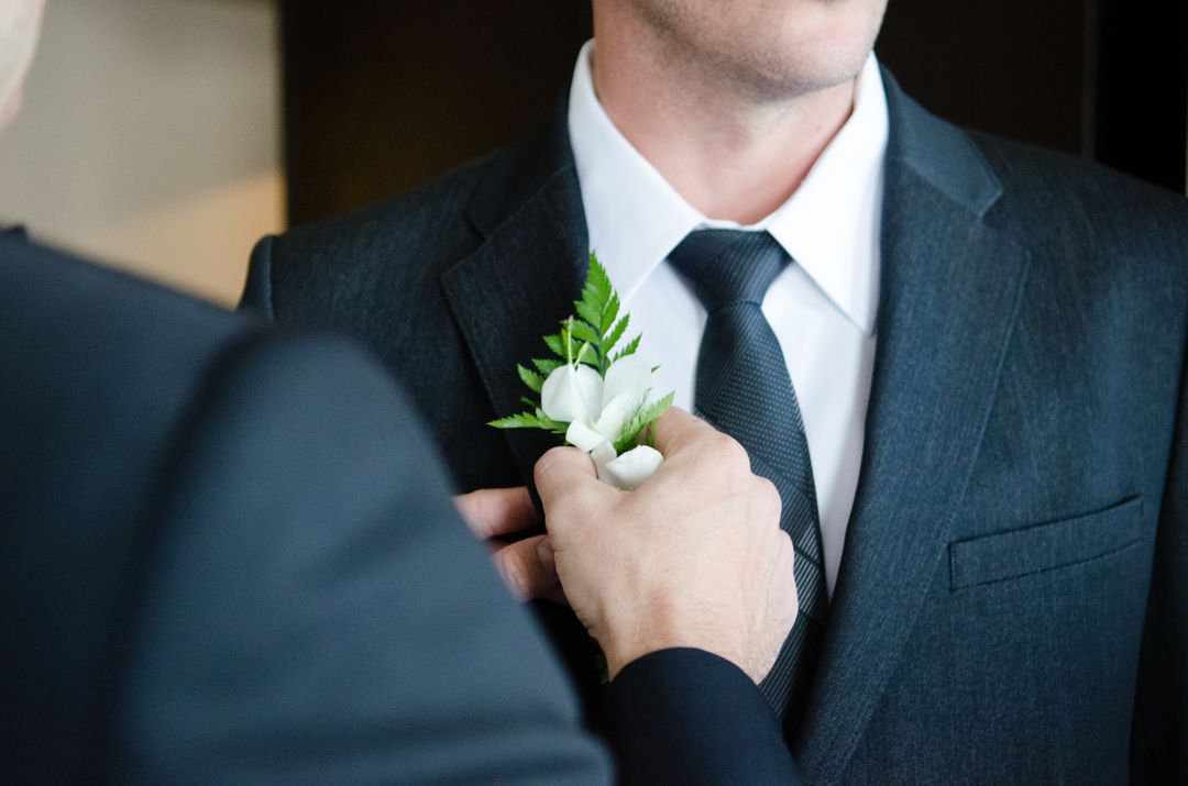 image of a man on his wedding day getting a white flower placed on his suit