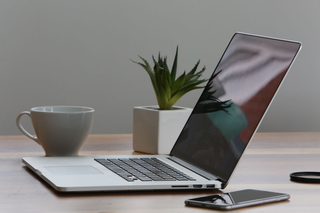 Image of a Laptop and a Cup on a Desk with a Plant in the Background
