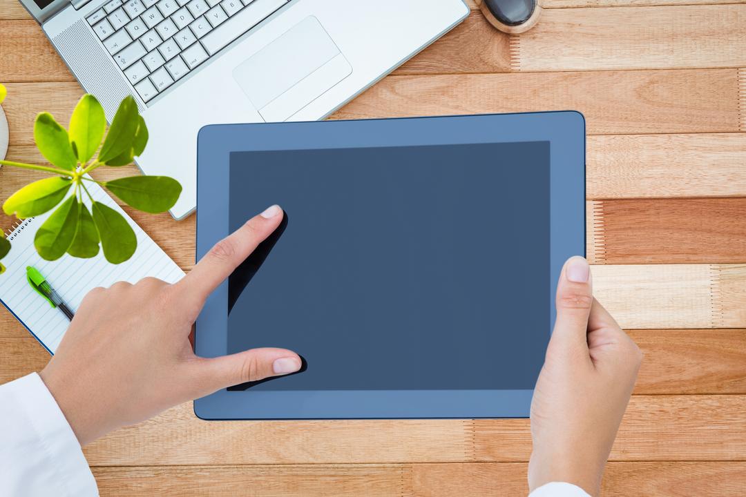 Image of a Person Holding a Tablet and a Laptop on a Desk in the Background