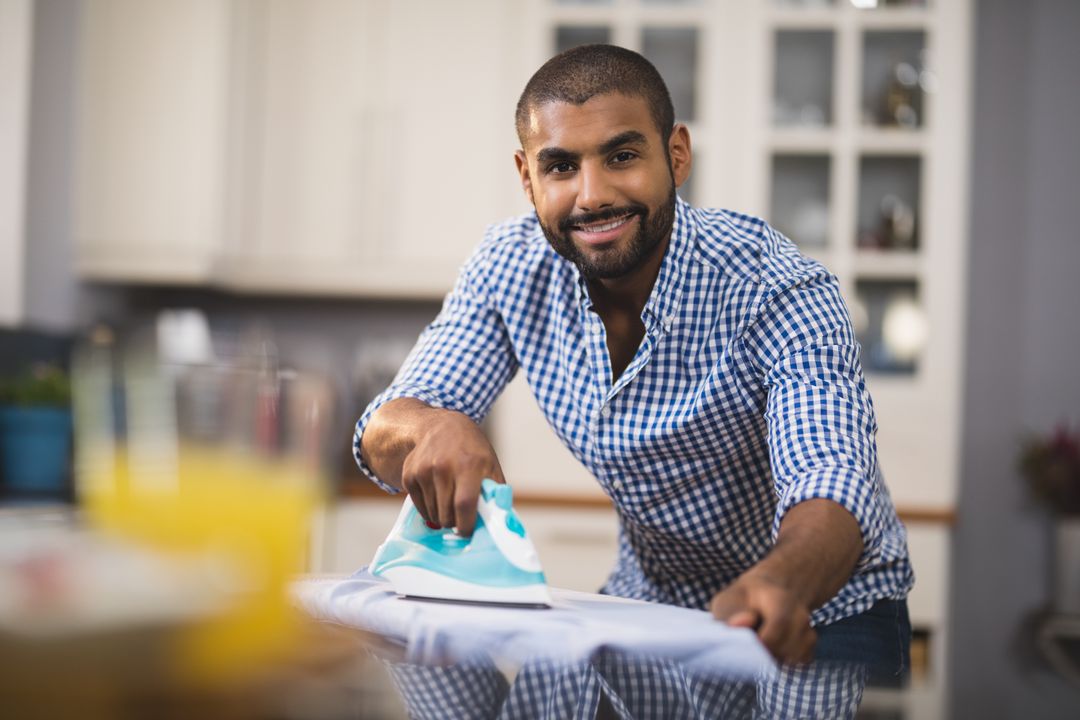 Portrait of smiling young man ironing cloth in kitchen from Pikwizard