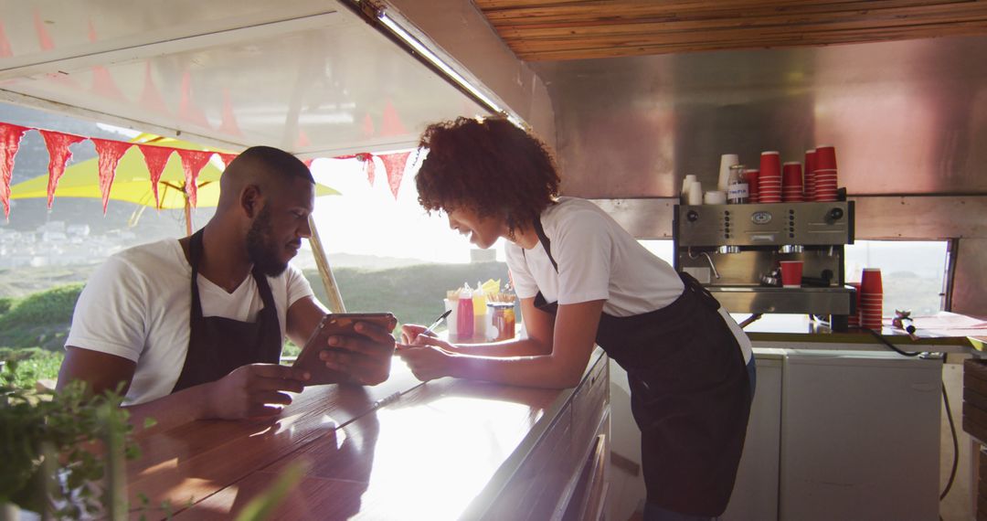 African american couple wearing aprons using digital tablet and taking notes in the food truck - Free Images, Stock Photos and Pictures on Pikwizard.com