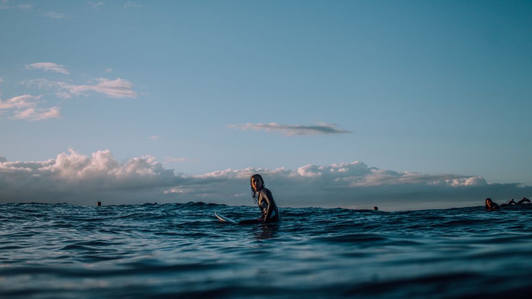 Photograph of woman sitting on surfboard in the ocean