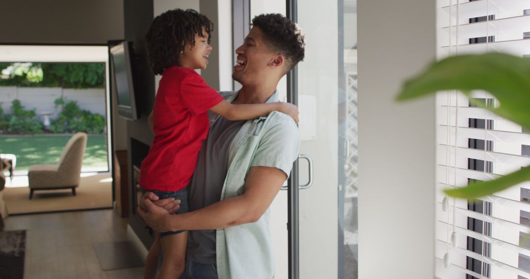 African american father carrying his son smiling while standing at home - Free Images, Stock Photos and Pictures on Pikwizard.com