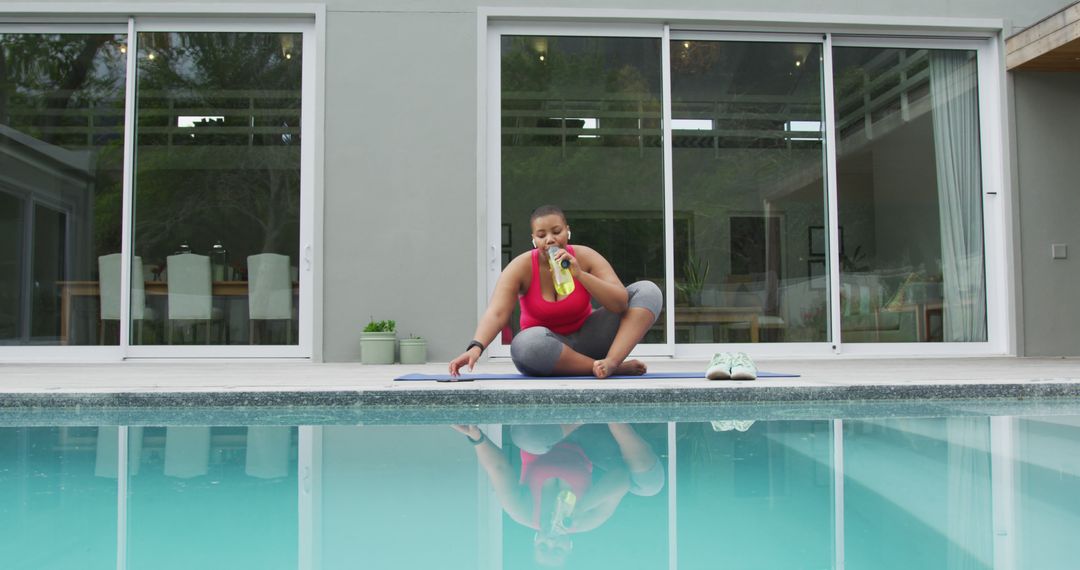 Happy african american plus size woman practicing yoga, stretching next to  swimming pool in garden from Pikwizard