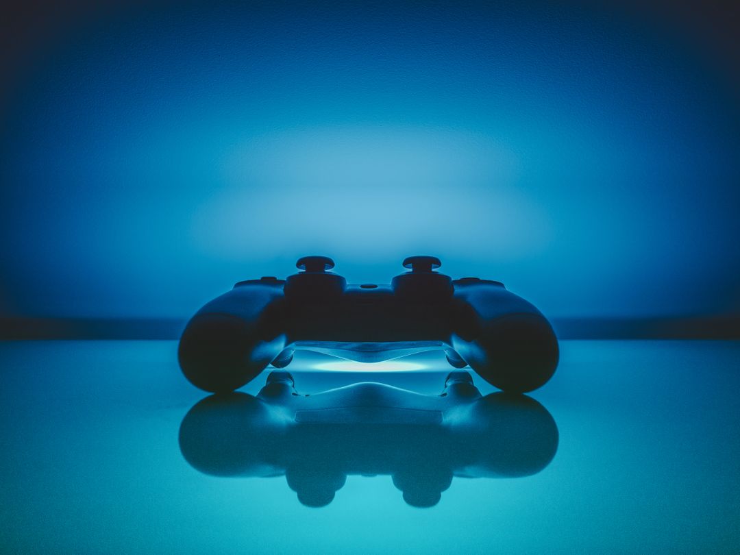 Lit Playstation controller placed on a reflective surface, blue hue from controller