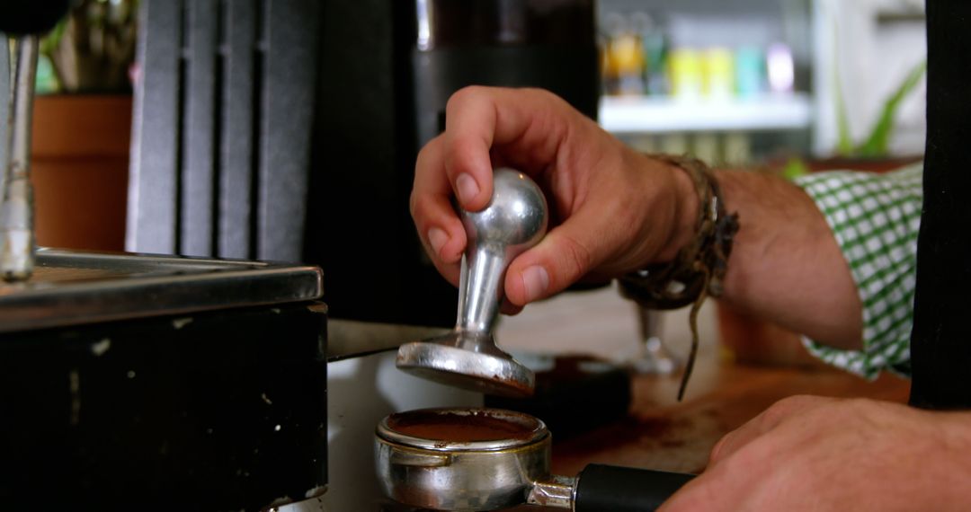 Waiter using a tamper to press ground coffee into a portafilter in cafe 4k  from Pikwizard