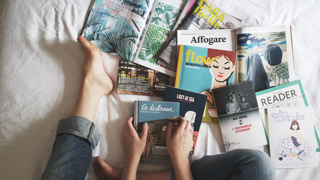 Woman sitting on a bed surrounded with print magazines ads