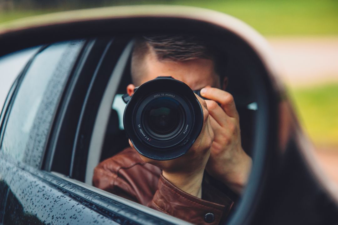 Photograph if a fashionable man taking a photo with a camera in car mirror