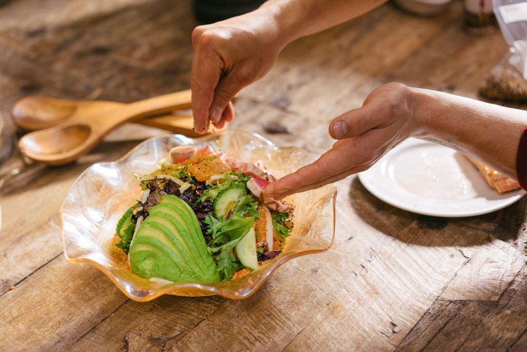 A person dresses a salad in a glass bowl on a wooden table - Why you might consider starting a food blog - Image
