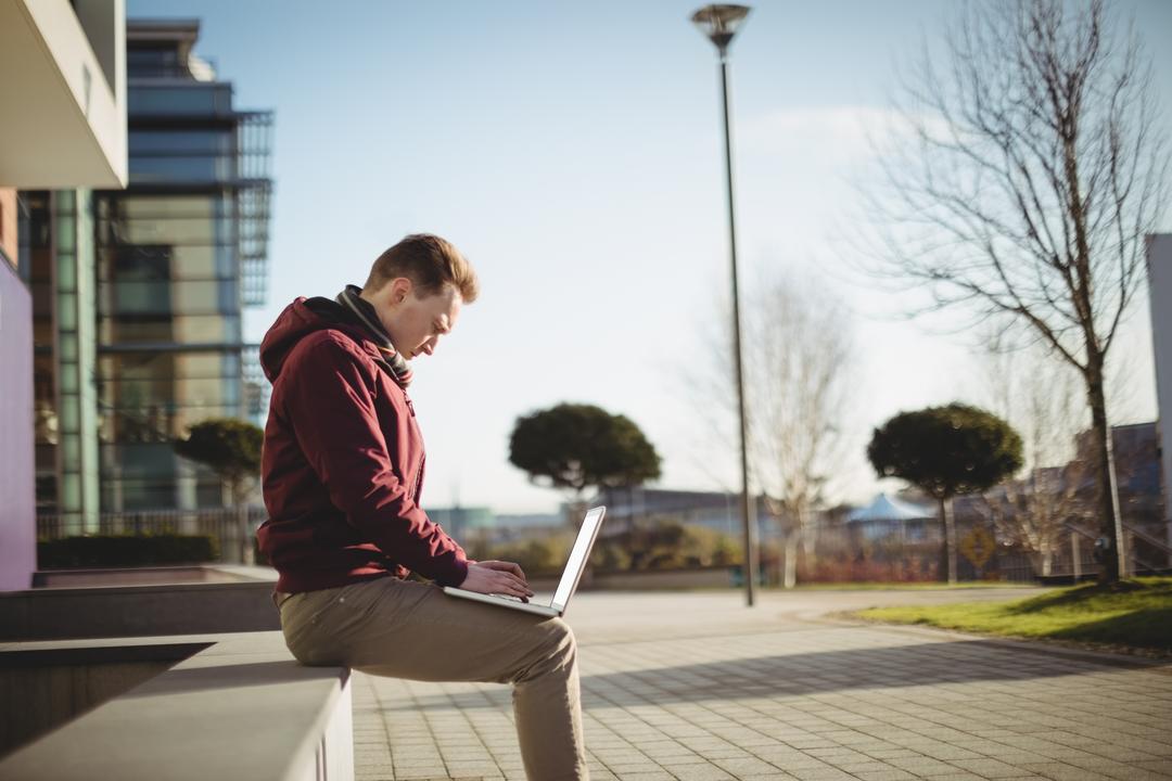 Man sitting on a wall typing onto his laptop in urban area - Essential steps to start a lifestyle blog and be successful - Image