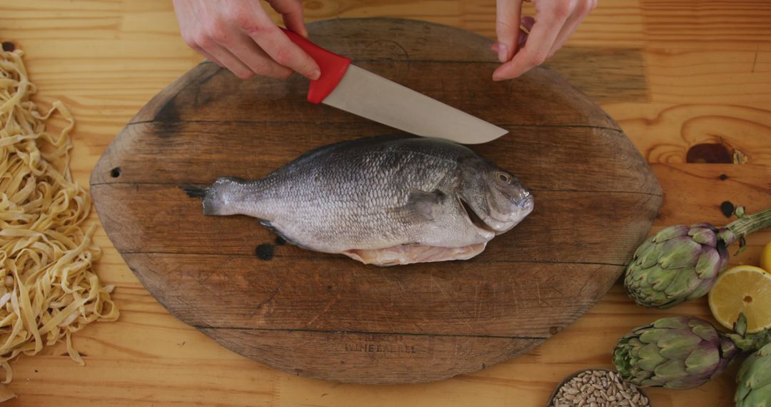 Hands of caucasian female cook slicing fish on cutting board in kitchen  from Pikwizard