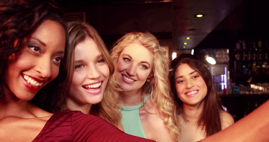 A diverse group of young women are taking a selfie together, smiling  brightly in a bar setting from Pikwizard