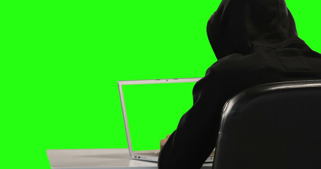 A person in a black hoodie is using a laptop against a green screen  background, with copy space from Pikwizard