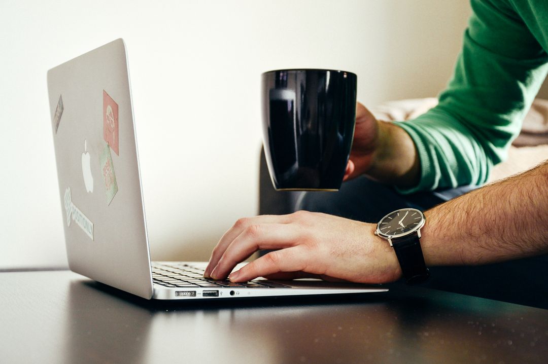 Side image of a person wearing a watch and holding a mug while typing copy